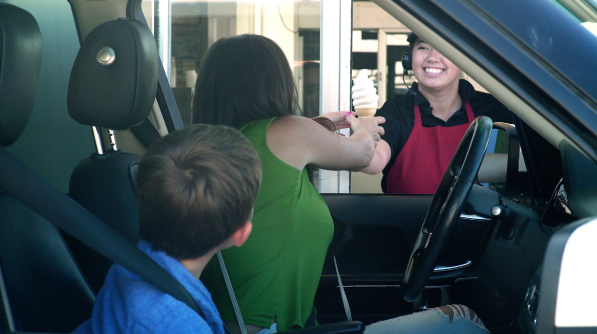 A cheerful, smiling server delivering ice-cream to a mother and her child as an example of great customer service